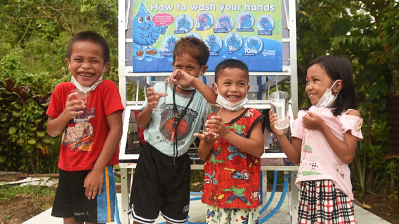 Children in front of a hand washing instruction sign, drinking water and laughing.